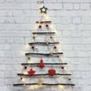 Weihnachtsbaum aus Stöcken und Ästen gegen eine weiße Ziegelwand. Der Baum besteht aus Stöcken und Ästen unterschiedlicher Länge, die in einer dreieckigen Form angeordnet sind. Der Baum ist mit roten und goldenen Kugeln, roten Herzen und goldenem Lametta